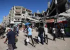 فلسطينيون يمرون أمام مبنى مدمر في سوق مؤقت بمخيم النصيرات للاجئين وسط قطاع غزة