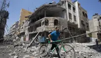 رجل فلسطيني يدفع دراجته وسط الركام في أعقاب غارة عسكرية إسرائيلية على مدينة غزة ، في 23 يوليو / تموز 2014. © أ ف ب/أرشيف