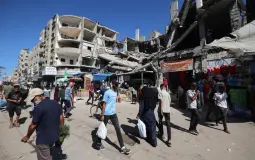 فلسطينيون يمرون أمام مبنى مدمر في سوق مؤقت بمخيم النصيرات للاجئين وسط قطاع غزة