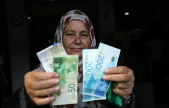 سيدة من غزة تحمل عملة الشيكل