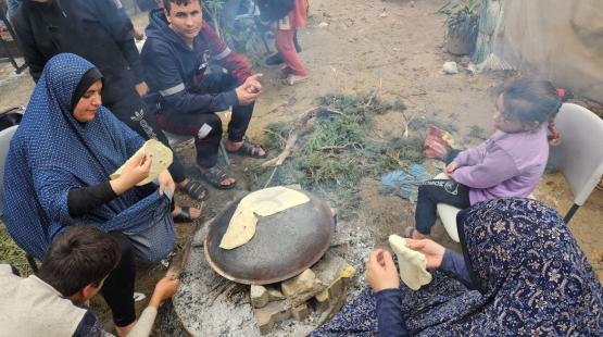 فلسطينيات نازحات يعددن ما يسمى شعبيا "خبز الصاج" في مخيم للنازحين غرب مدينة رفح أقصى جنوب قطاع غزة على الحدود مع مصر (الجزيرة)