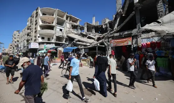فلسطينيون يمرون أمام مبنى مدمر في سوق مؤقت بمخيم النصيرات للاجئين وسط قطاع غزة