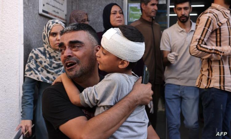 رجل فلسطيني يحمل صبيًا بعد أن عولج من إصابة في الرأس في المستشفى، في أعقاب غارة جوية إسرائيلية على رفح بجنوب قطاع غزة في 23 أكتوبر 2023.