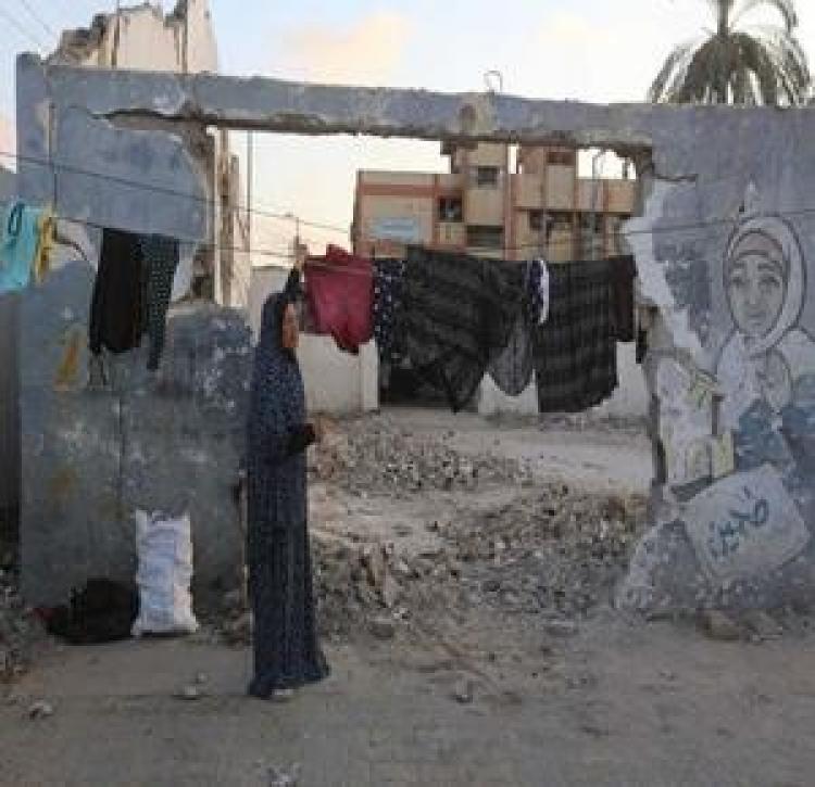 سيدة فلسطينية تنشر الغسيل على حطام منزلها