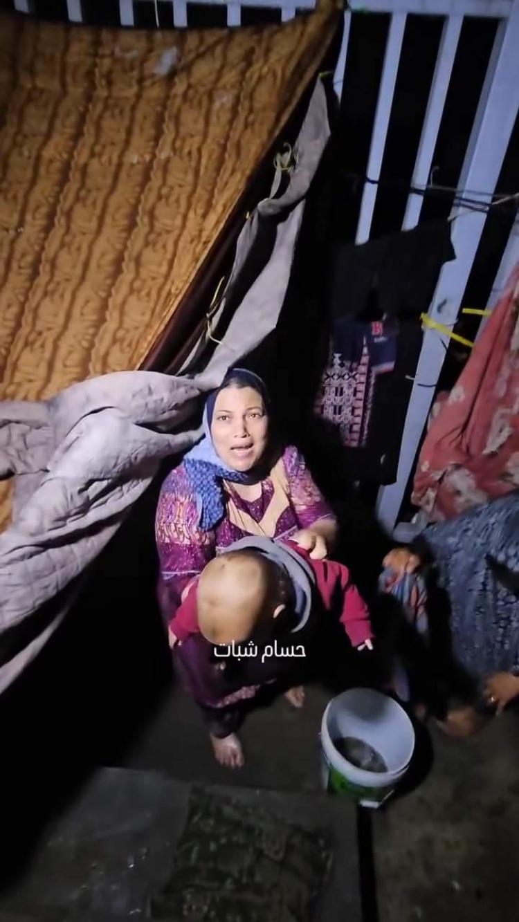 سيدة تحمل طفلها عقب غرق الخيمة جراء مياه الأمطار