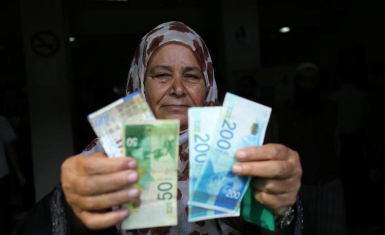 سيدة من غزة تحمل عملة الشيكل