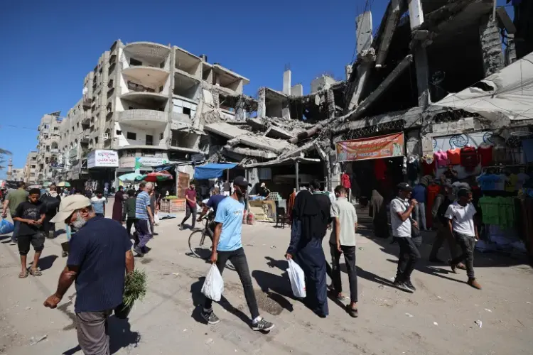 فلسطينيون يمرون أمام مبنى مدمر في سوق مؤقت بمخيم النصيرات للاجئين وسط قطاع غزة